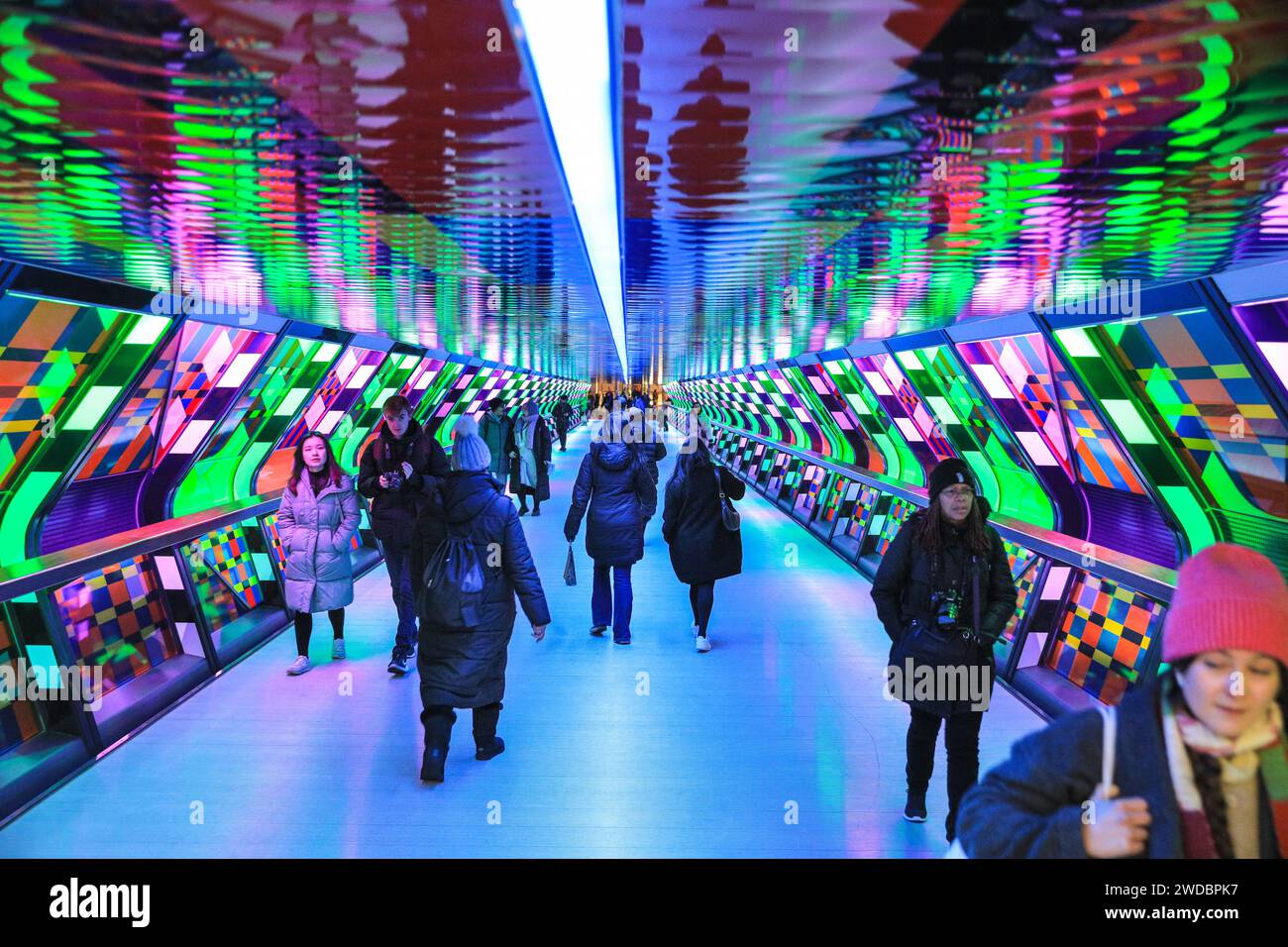 London, Großbritannien. Januar 2024. Die Leute laufen entlang, schauen sich die „von der Farbe faszinierte“ von Camille Walala (Frankreich) auf der Adams Plaza Bridge an und machen Fotos. Die jährlichen „Winter Lights“ sind spektakuläre Lichtinstallationen und immersive Kunst rund um Canary Wharf in East London. Quelle: Imageplotter/Alamy Live News Stockfoto