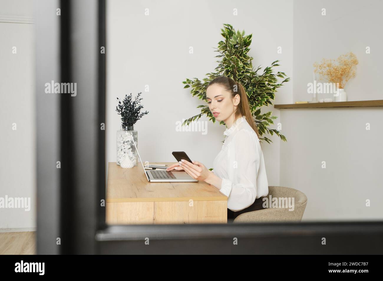 Blick durch das Fenster einer Frau, die in einem hellen Büro arbeitet Stockfoto