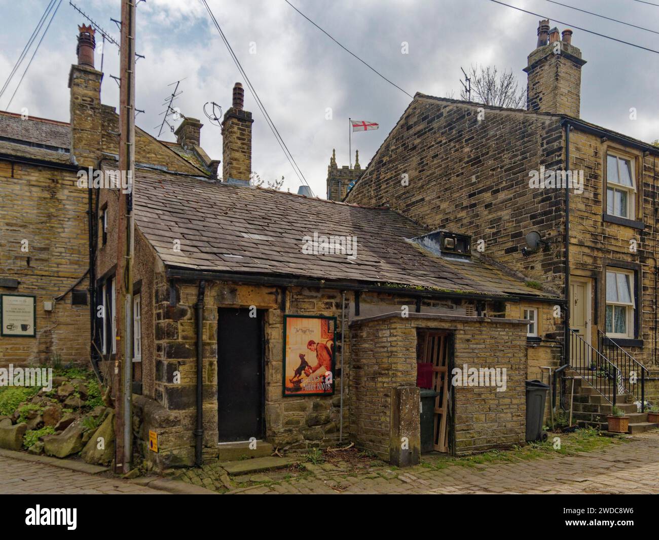 Ein rustikales altes Gebäude mit einem Poster an der Wand und einer englischen Flagge im Hintergrund, Old House in Haworth. Bronte Country. England, Großbritannien Stockfoto