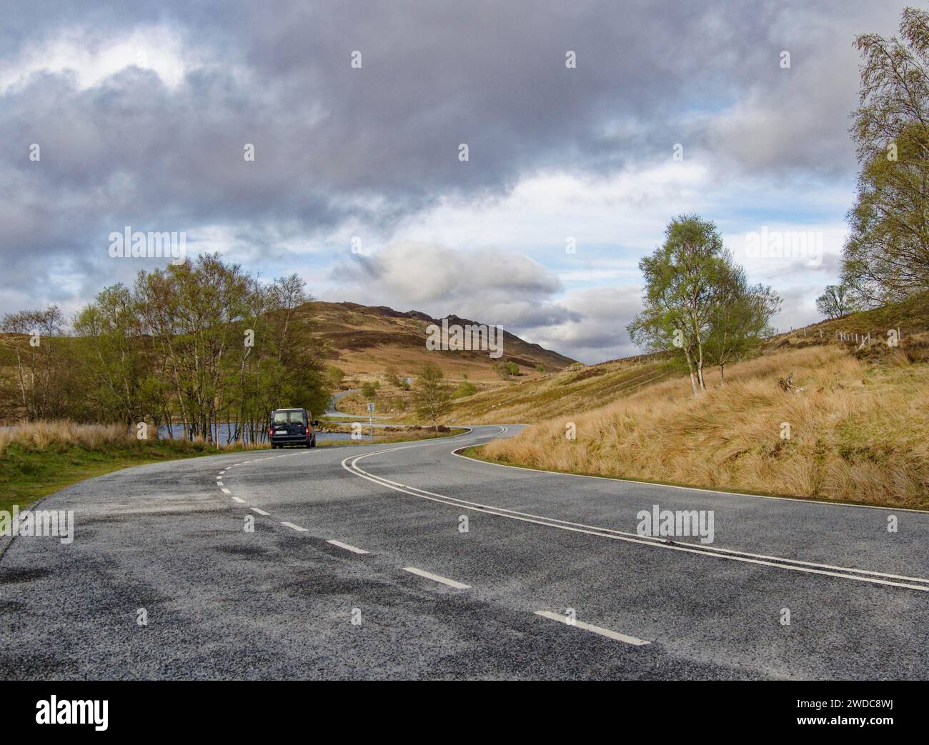 Eine kurvige Landstraße schlängelt sich mit einem Bus durch eine herbstliche Landschaft. Schottland, Großbritannien Stockfoto