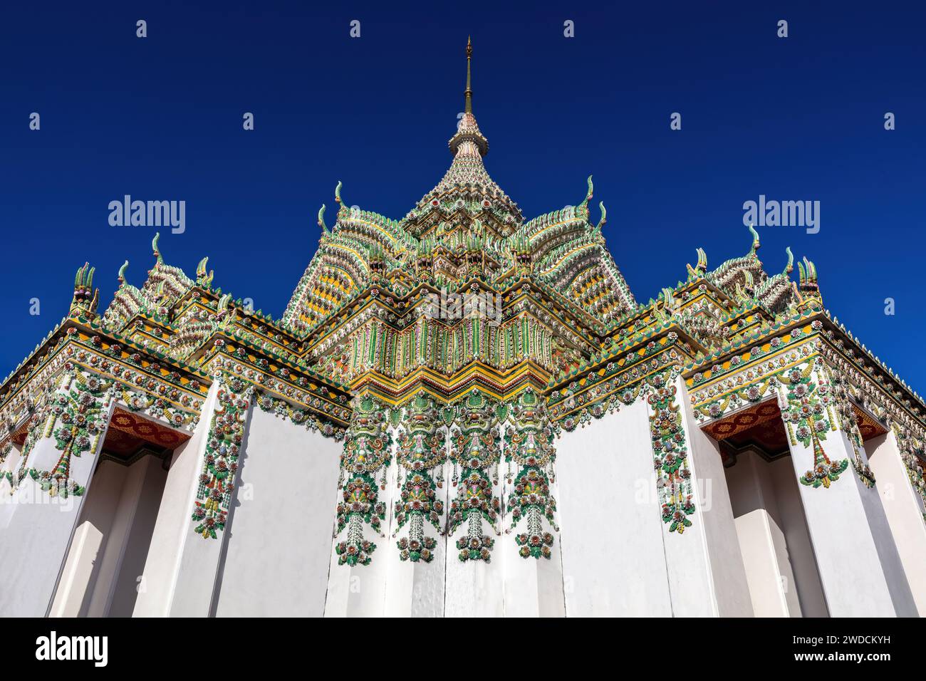 Tempelgebäude auf dem Gelände von Wat Po, Bangkok, Thailand. Außen mit weißen Wänden; farbenfrohe und komplizierte Verzierungen auf dem Dach. Blauer Himmel oben. Stockfoto