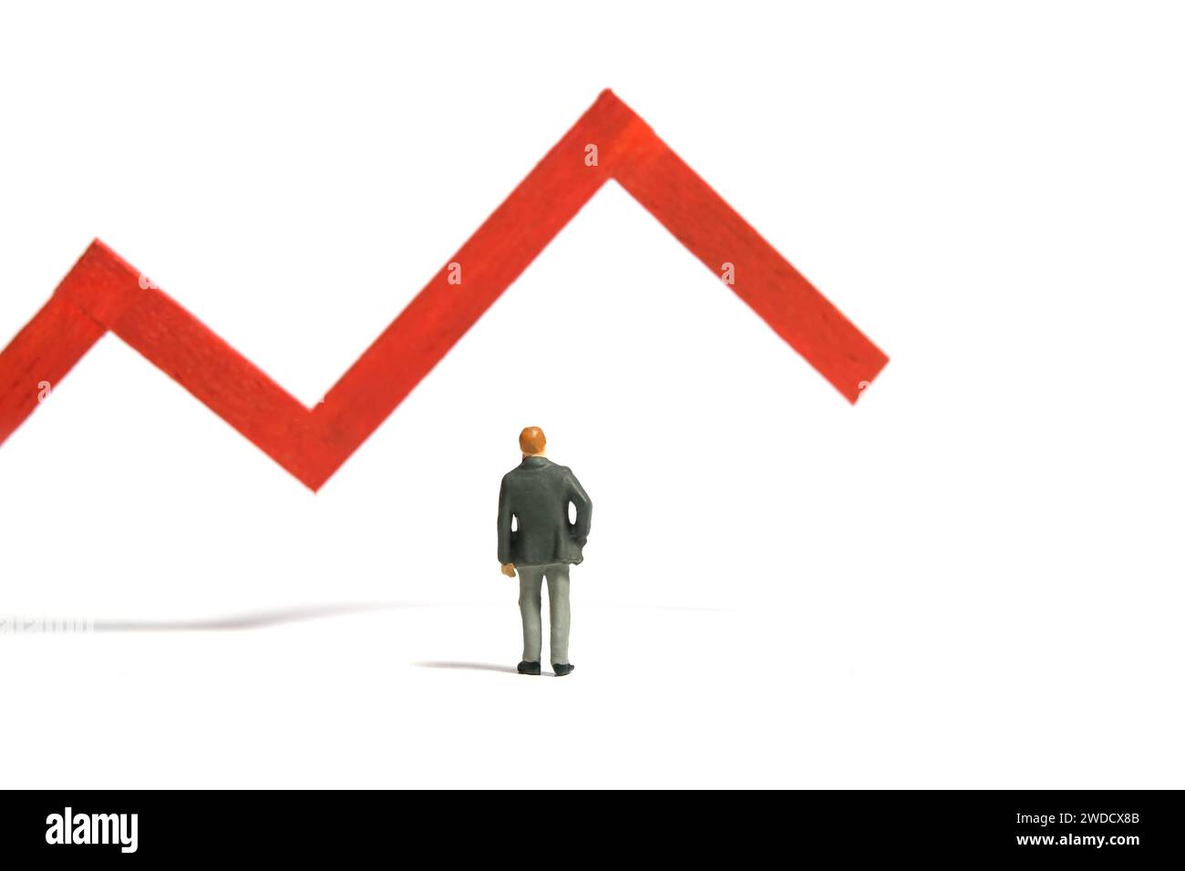 Miniatur-Kleinkinder-Spielfiguren-Fotografie. Investitionsausfall- und Verlustkonzept. Ein Geschäftsmann, der vor einem roten Balken steht, der abwärts geht. Isolieren Stockfoto