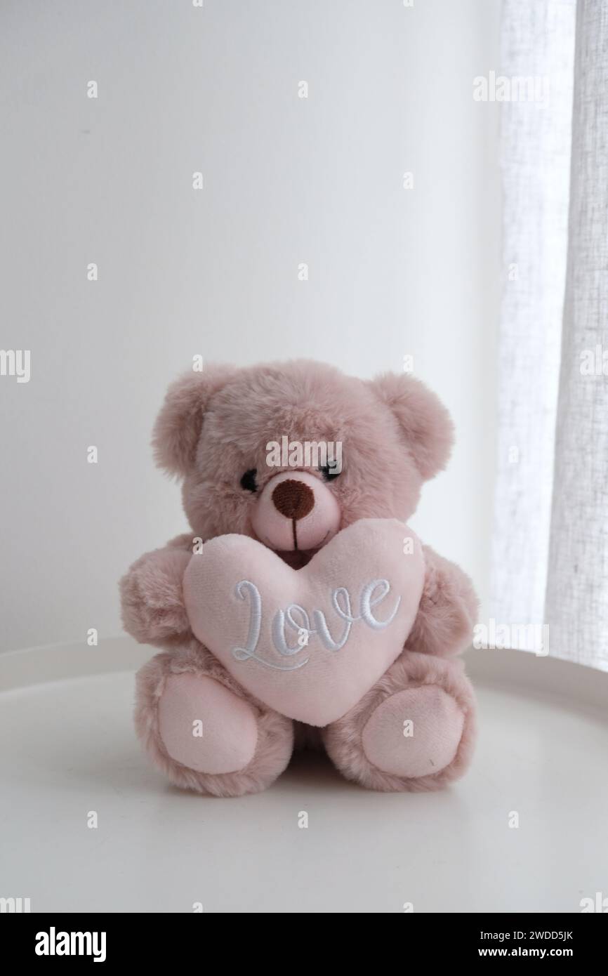 Ein romantischer rosafarbener Teddybär, der ein Herz der Liebe auf dem Tisch hält Stockfoto