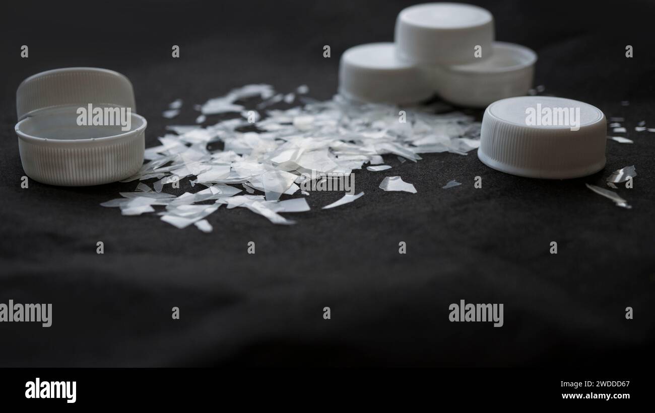 Makroaufnahme auf einem Stapel aufgelöster Mikroplastikpartikel neben Plastikflaschenverschlüssen und Müllbeuteln. Altes zersetztes und zerbrochenes Mikroplastik Stockfoto