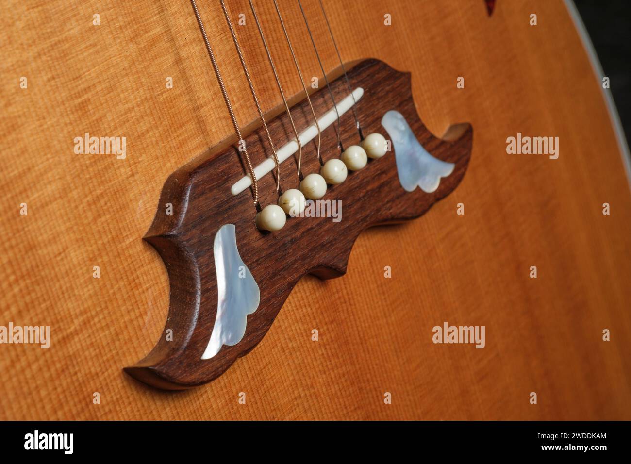 Akustikgitarrenbrücke mit Perlmutteinlage und Gitarrensaiten Stockfoto
