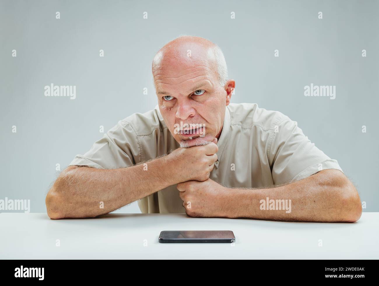 Mann, der das Kinn packt, die Augen auf das Smartphone fixiert, sichtbar verärgert über ein enttäuschendes digitales Erlebnis Stockfoto