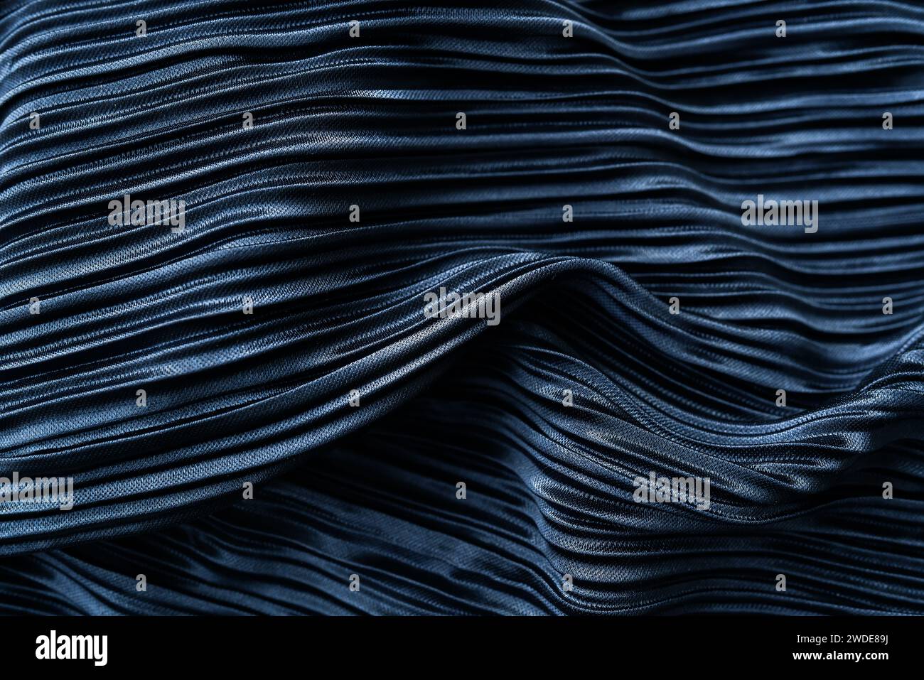 Ein dunkelblauer Faltenstoff mit glänzender Textur und komplizierten Falten. Es hat ein künstlerisches Gefühl durch das Spiel von Licht und Schatten auf den Falten Stockfoto