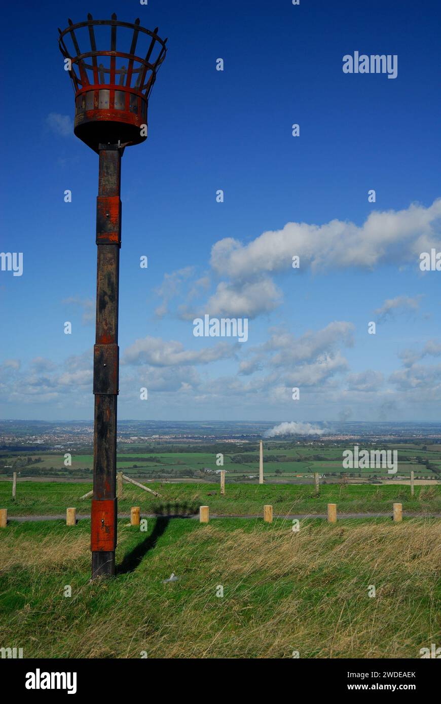 Feuerleuchte auf der Spitze des Westbury Hill, Wiltshire, mit dem ehemaligen Schornstein der Zementfabrik im Hintergrund (2016 abgerissen). Stockfoto