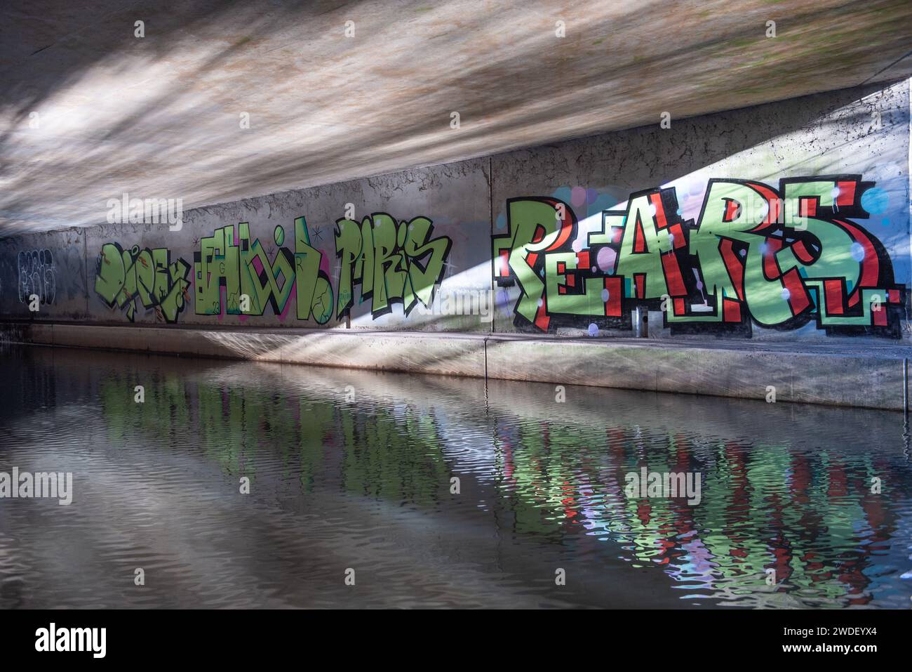 Graffiti-Schrift an den Wänden des Kanaltunnels, mit Wasserreflexionen Stockfoto