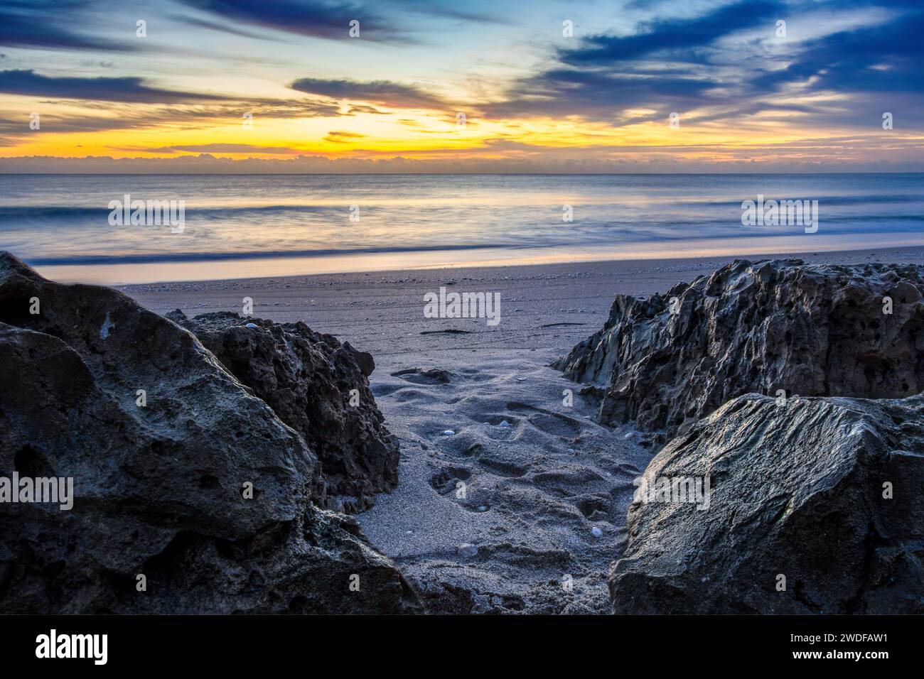 Dynamischer Sonnenaufgang an der Küste mit strukturierten Felsen und weichem Sand, ideal für dynamische Website-Header, Reisezeitschriften und inspirierende Poster. Stockfoto