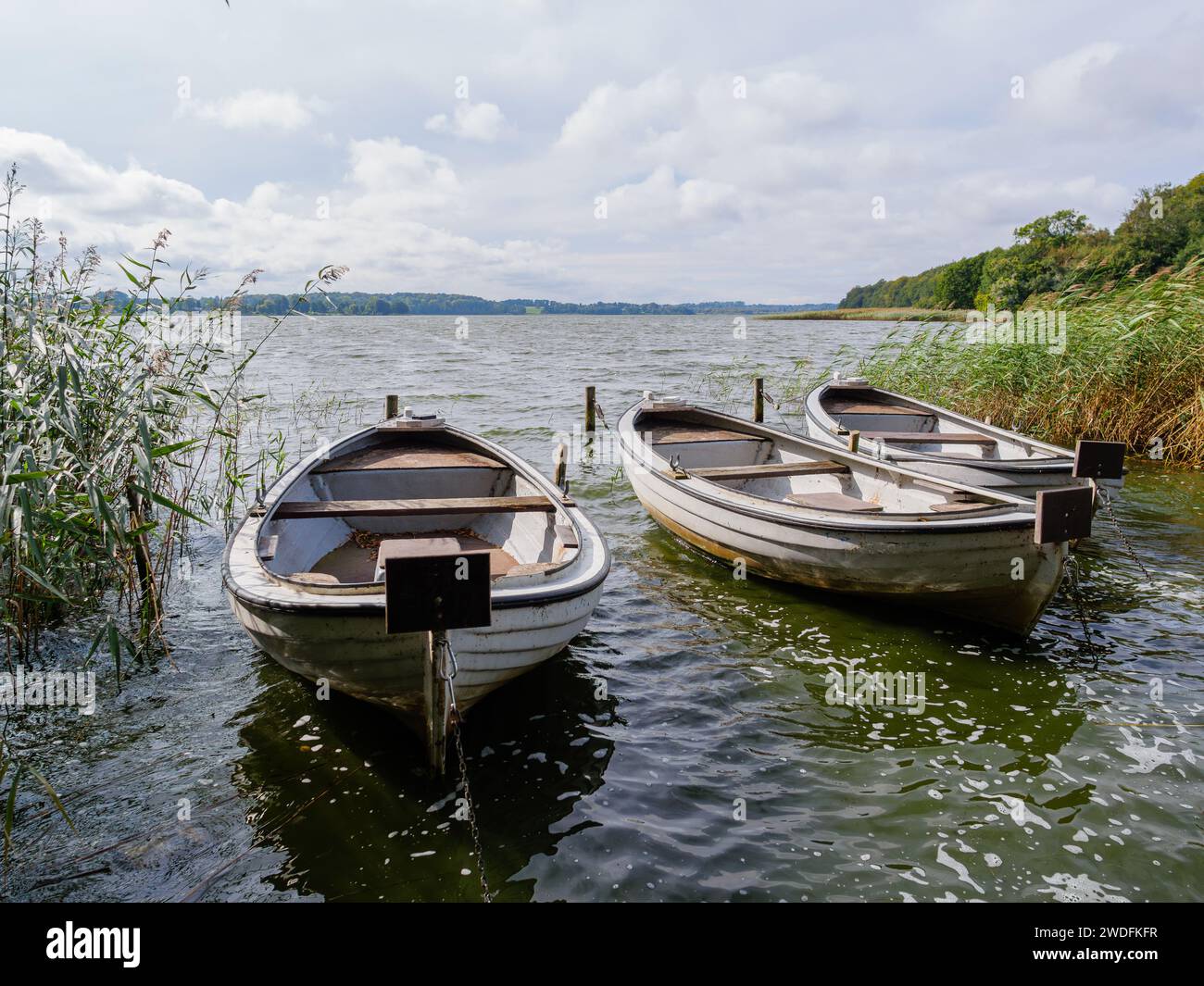 Drei weiße Ruderboote, die an einem hellen, sonnigen und windigen Tag in einem großen See vor Anker liegen Stockfoto