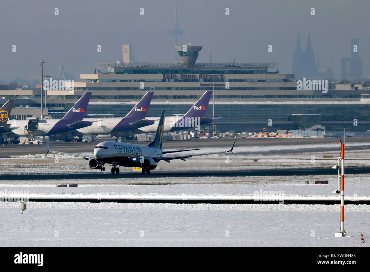 Eine Maschine von Ryanair startet am Köln Bonn Airport - im Hintergrund Cargomaschinen von FedEx und das Hauptgebäude mit Kölner Dom. Nach starkem Schneefall wirkt sich das Wetter auch auf den Flugbetrieb am Flughafen Köln/Bonn aus. Der kontinuierliche Winterdienst mit Räumfahrzeugen machen die Taxiways und Lande- und Startbahnen wieder benutzbar. Themenbild, Symbolbild Köln, 20.01.2024 NRW Deutschland *** Ein Ryanair-Flugzeug startet am Flughafen Köln Bonn im Hintergrund FedEx Frachtflugzeuge und das Hauptgebäude mit Kölner Dom nach starkem Schneefall wirkt sich das Wetter auch auf den Flugbetrieb aus Stockfoto