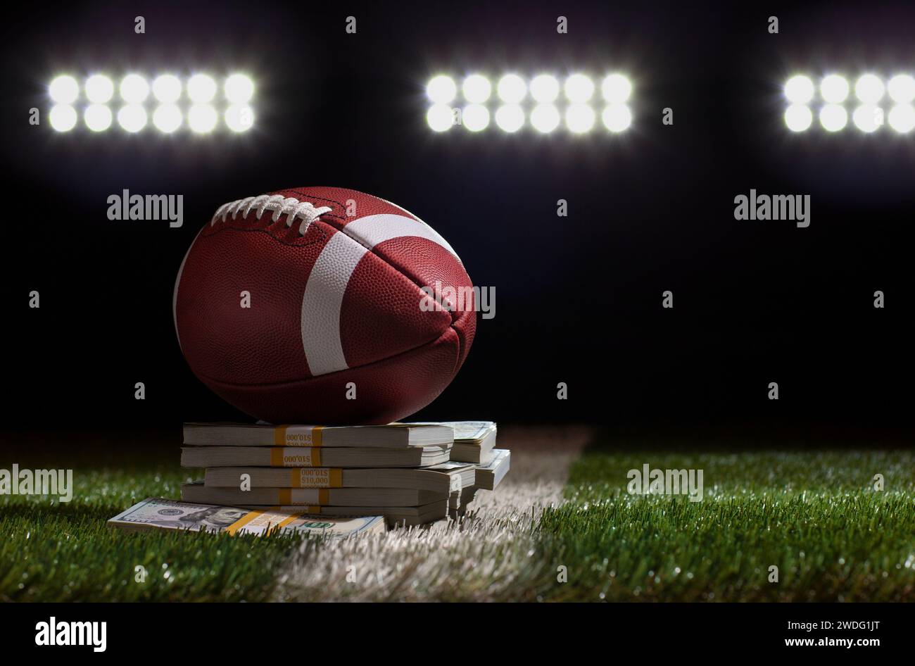 Niedriger Blickwinkel auf einen Fußball, der auf einem Haufen Geld auf einem Rasenfeld unter Stadionlichtern sitzt Stockfoto