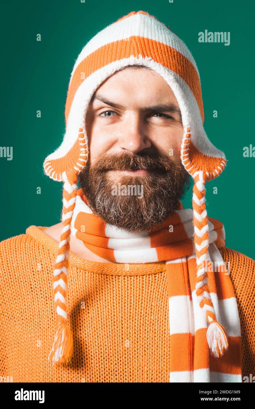 Nahaufnahme Porträt eines attraktiven Mannes mit Bart und Schnurrbart in orangefarbenem Pullover, lustigem Hut und gestreiftem Schal. Schöner bärtiger Mann in warmen Kleidern Stockfoto