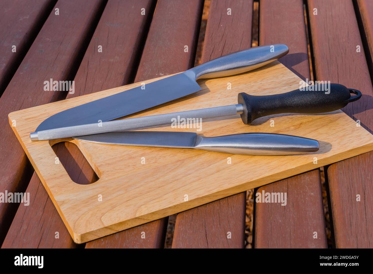 Kochmesser, Steakmesser und Honig-Stahl auf Holzbrett auf Picknicktisch Stockfoto