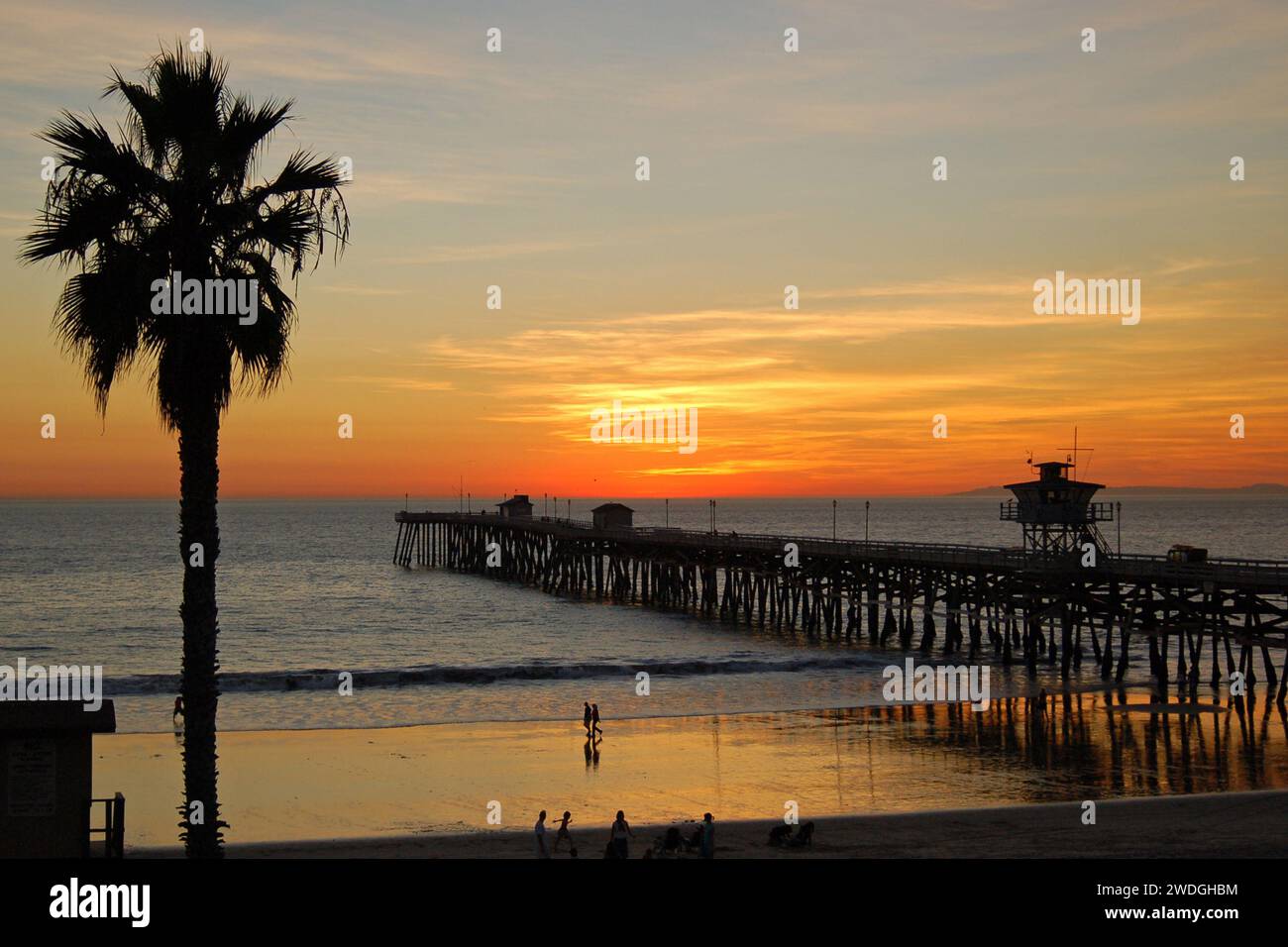 Am Strand und Pier in San Clemente entwickelt sich ein wunderschöner Sonnenuntergang, der die Palmen und Menschen in Silhouette bringt Stockfoto