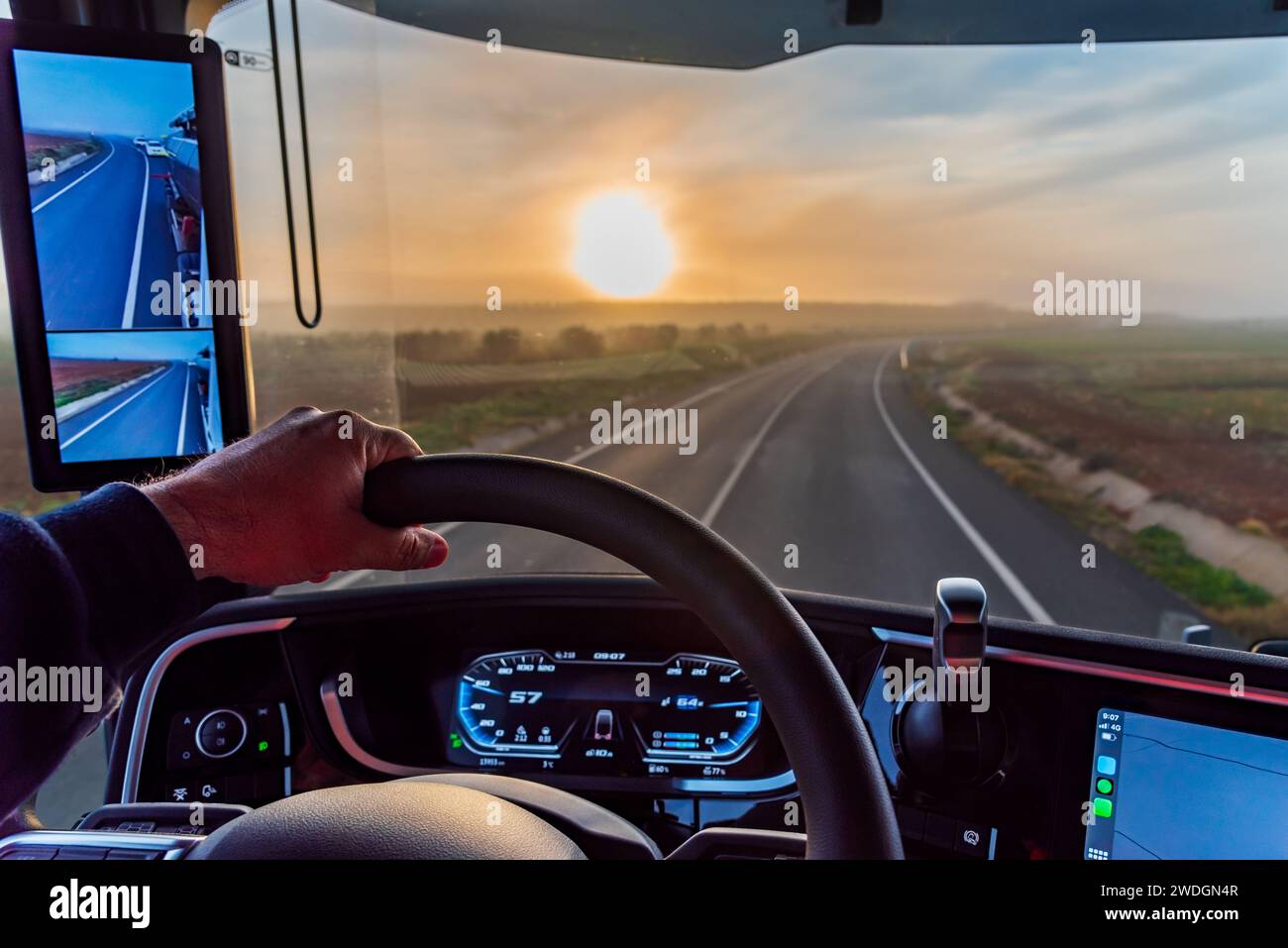 Blick vom Fahrersitz eines Lkws mit Rückspiegeln einer konventionellen Straße bei Sonnenaufgang. Stockfoto