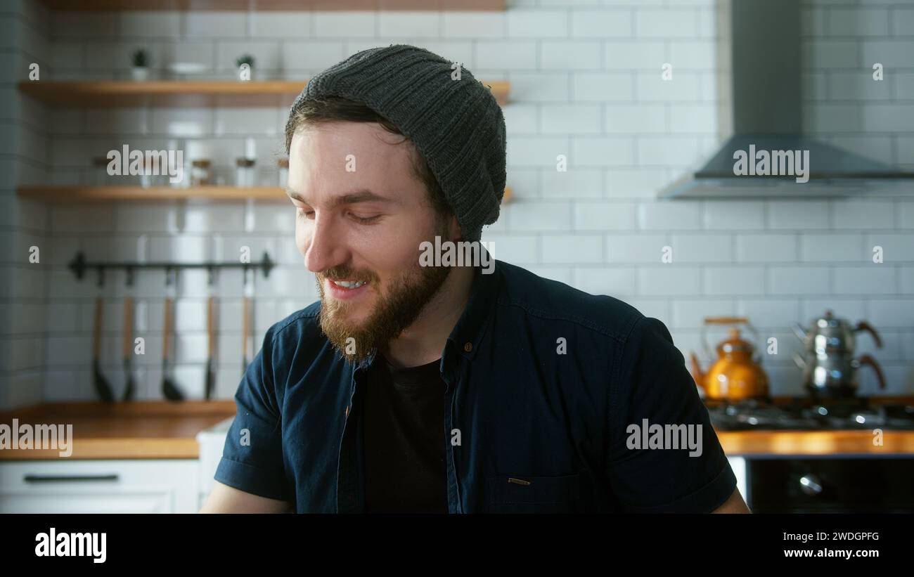 Porträt eines Geschäftsmannes mit Mütze, der in der modernen Küche zu Hause sitzt, spricht und Berichte in Videokonferenzgesprächen zeigt. Selbstbewusste Männer haben Video Co Stockfoto