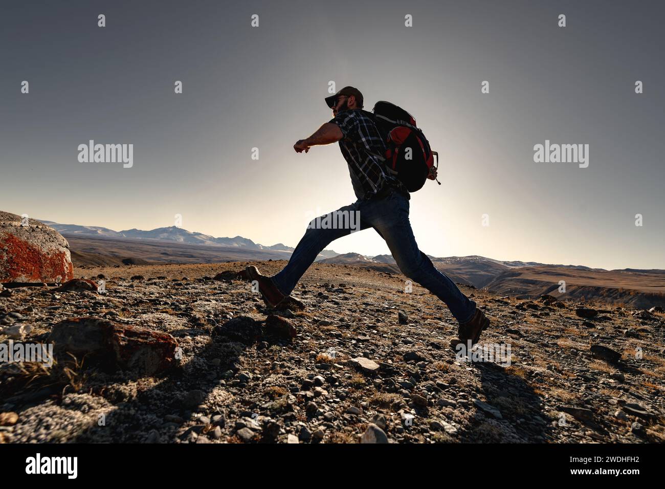 Aktiver Wanderer von Touristen mit Rucksack beschleunigt, bevor er in die Berge des Sonnenuntergangs springt Stockfoto