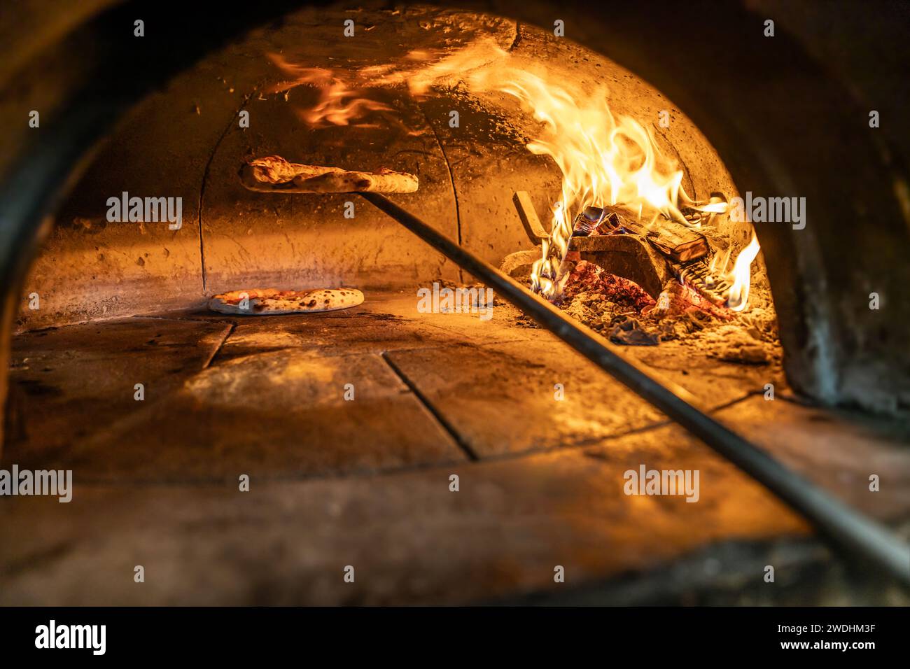 Traditioneller Ofen zum Backen von Pizza mit brennendem Holz und Schaufel. Neapolitanische Pizza wird auf einer Schaufel in einem Backofen fertig. Stockfoto