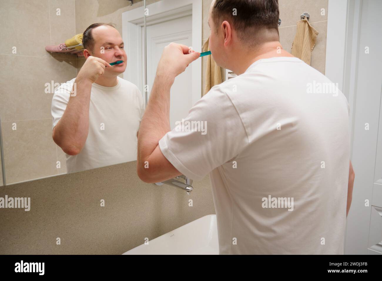 Ein Mann putzt sich die Zähne mit einer Zahnbürste im Badezimmer vor dem Spiegel. Übergewichtiger 40-jähriger Mann (vierzig) Stockfoto