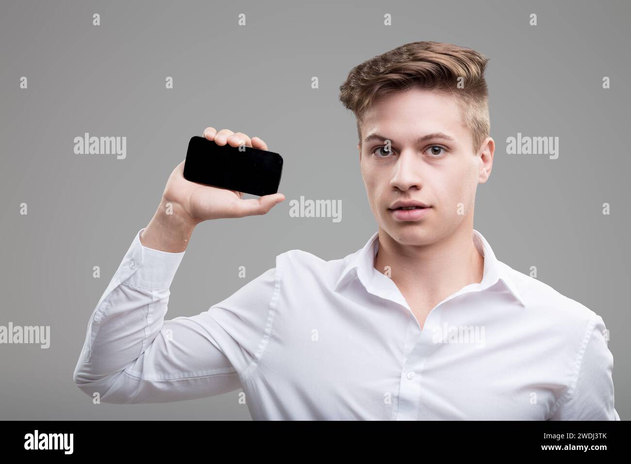 Der technisch versierte junge Profi in weißem Hemd hält das Smartphone und symbolisiert moderne Konnektivität und Stil Stockfoto