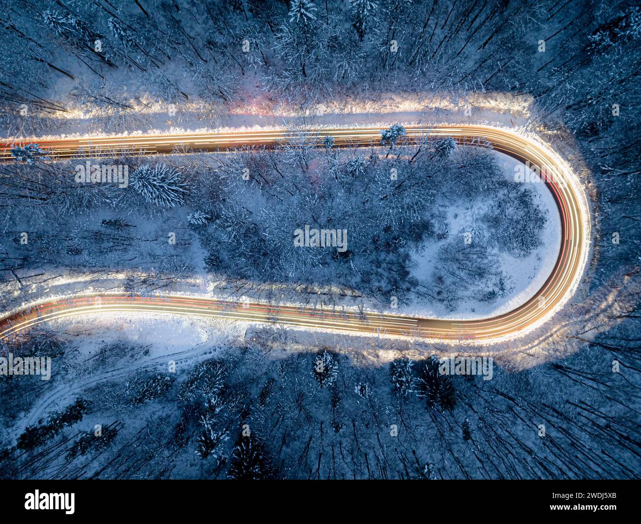 Verschwommene Lichter vorbeifahrender Autos auf kurvenreichen Straßen im Winter nach Einbruch der Dunkelheit. Transport im Winter bei Nacht. Stockfoto