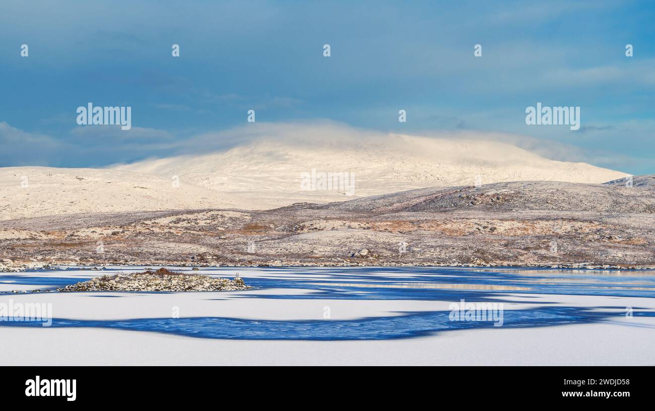 Gefrorenes blaues Wasser eines Sees mit schneebedeckten Hügeln, ungewöhnliches Wetter auf der hebridischen Insel South Uist, 2024, Äußere Hebriden, Schottland, Großbritannien Stockfoto