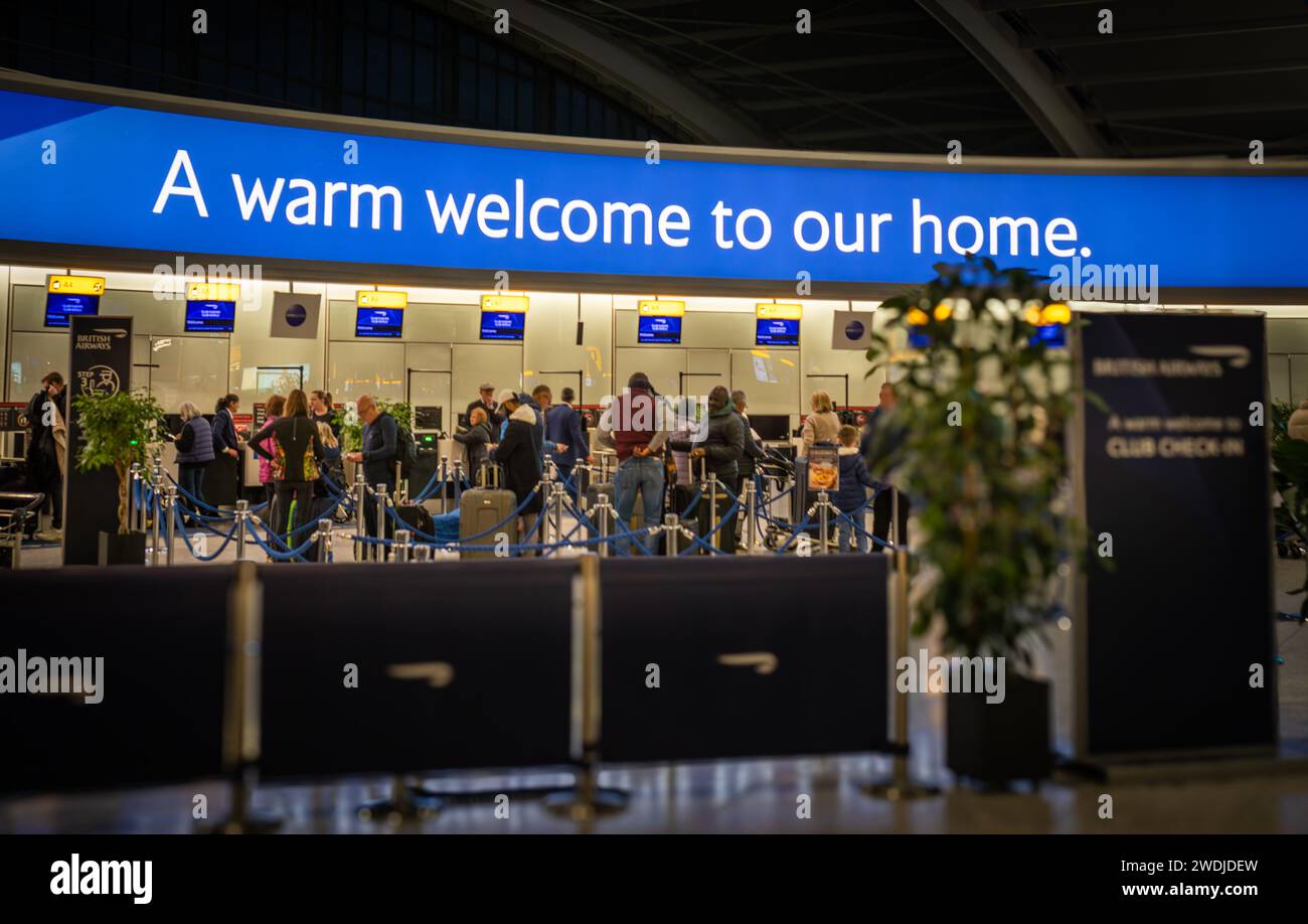 Passagiere stehen vor dem Check-in in der Business Class von British Airways unter einem großen beleuchteten Schild mit der Aufschrift „Ein herzlicher Willkommen in unserem Zuhause“ London Heathrow Air Stockfoto