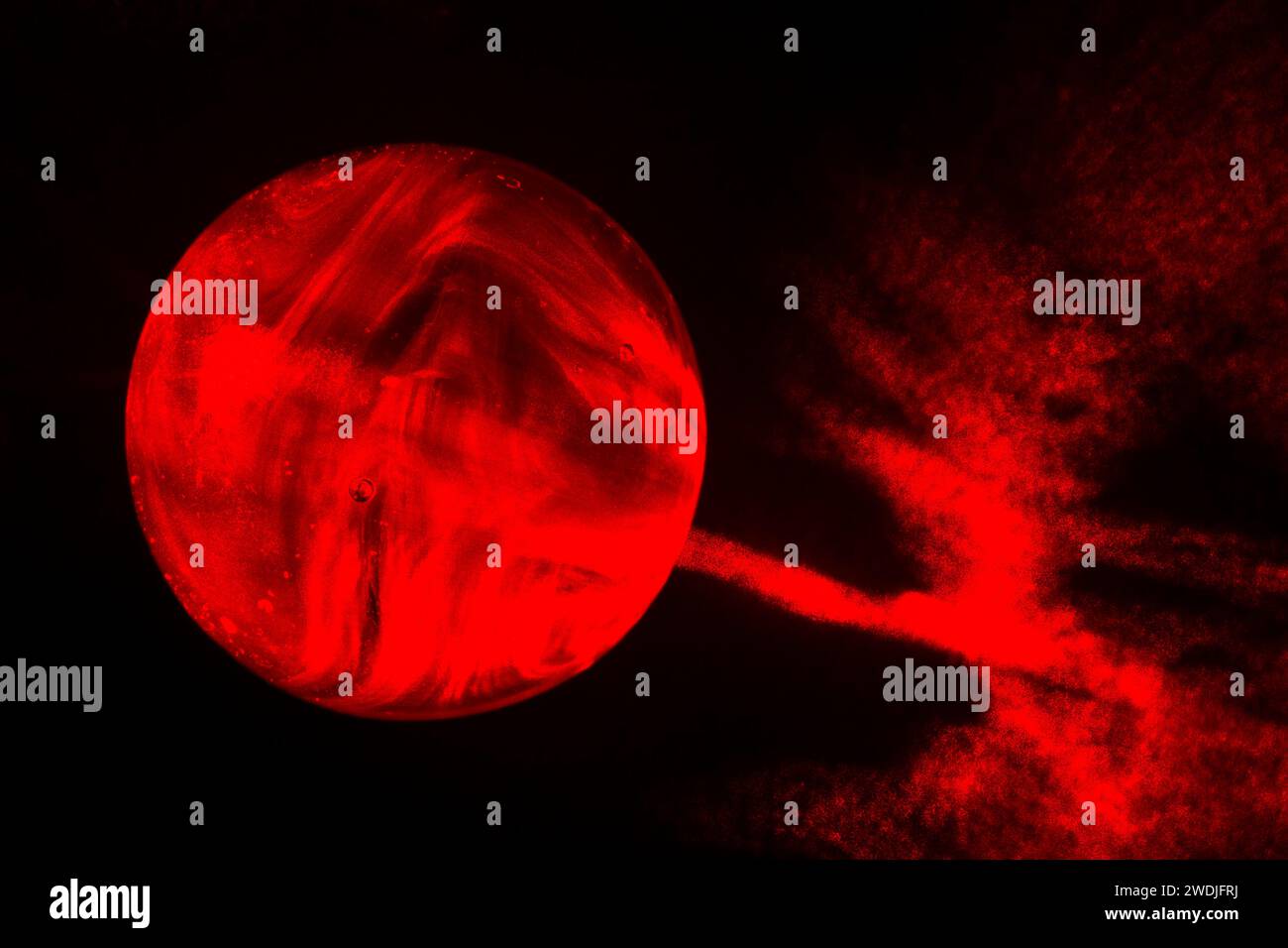 Ein roter Glasmarmor auf schwarzem Hintergrund, bemalt mit rotem Laserlicht. Stockfoto