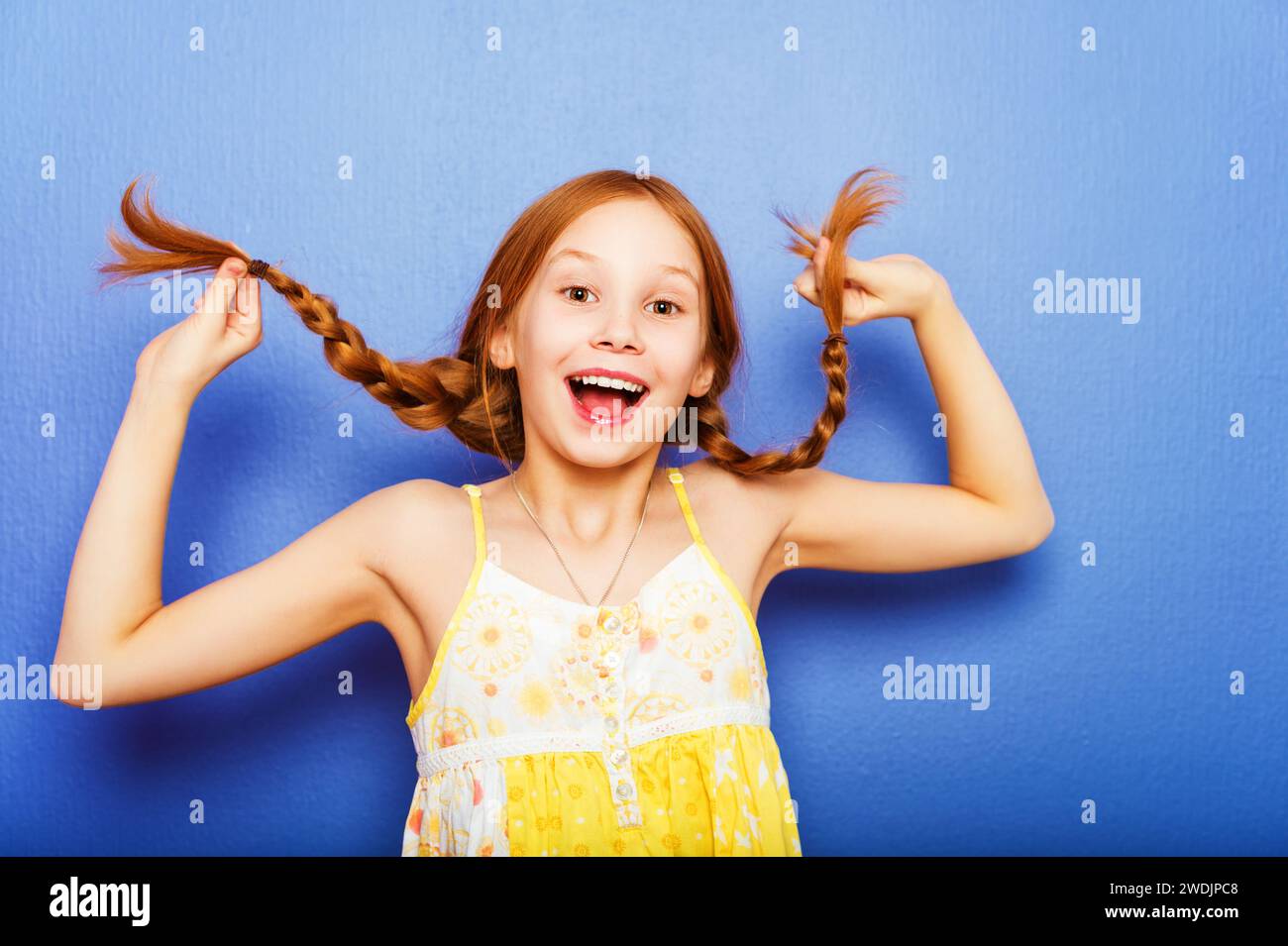 Studio-Aufnahme eines jungen 9-10-jährigen rothaarigen Mädchens mit gelbem Oberteil, das vor blauem lila Hintergrund steht Stockfoto