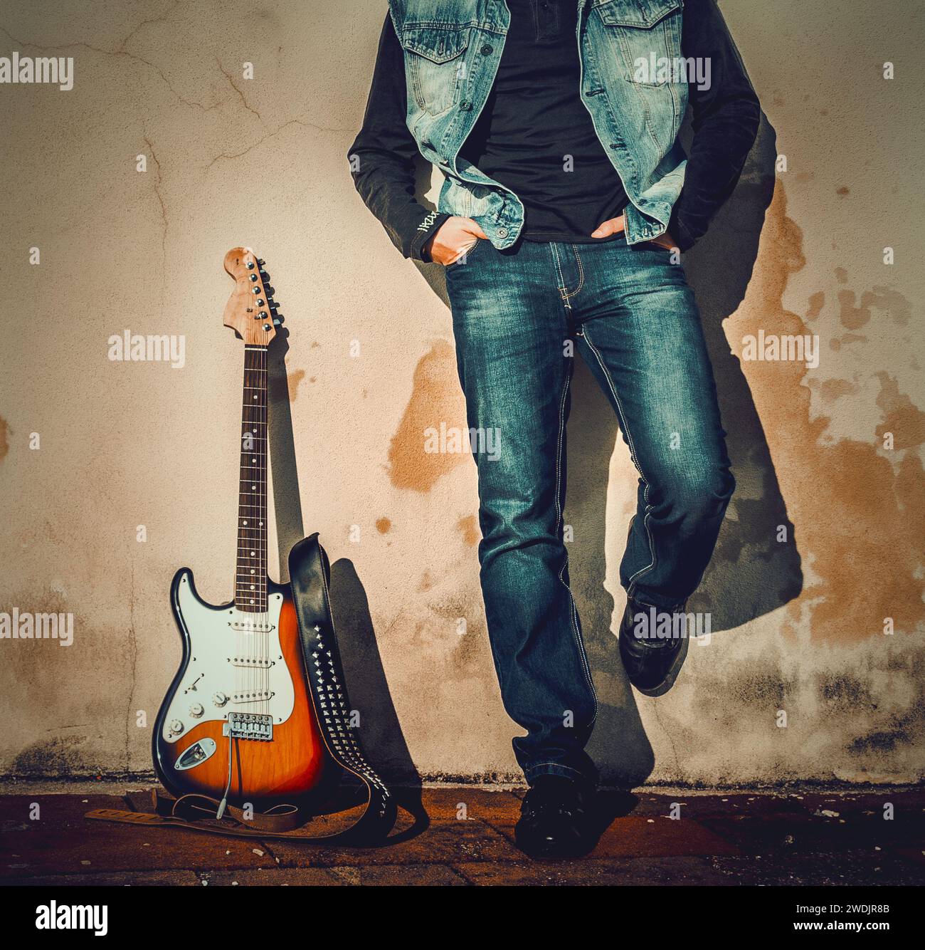 Vorderansicht eines Mannes und einer Gitarre, die auf einer Grunge-Wand gelehnt sind Stockfoto