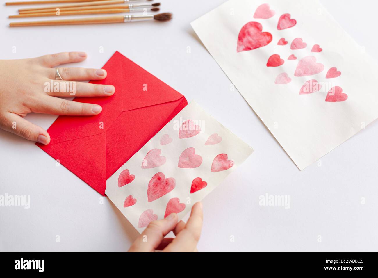 Eine Nahaufnahme einer Person, die zum Valentinstag Papierherzen mit Bleistiften auf einem Umschlag bastelt Stockfoto