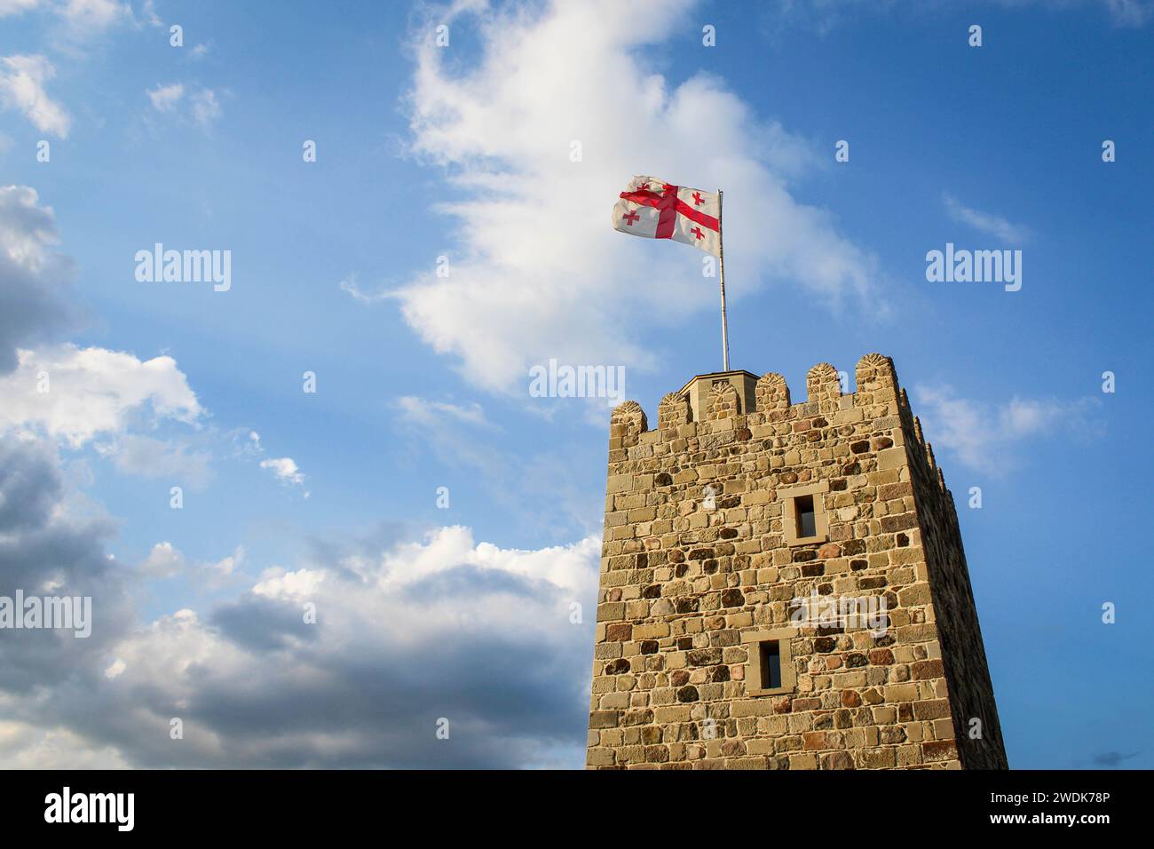 Die Nationalflagge von Georgien auf der Spitze des alten Steinturms winkt vor dem Hintergrund eines blauen Himmels mit Wolken. Festung Rabat, Akhaltsikhe. Verz Stockfoto