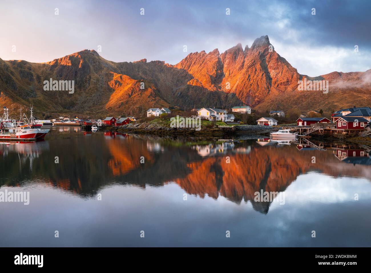 Reflexionen von Häusern und Bergen im Wasser im Dorf Ballstad während des Sonnenaufgangs, Vestvagoy, Nordland, Lofoten-Inseln, Norwegen, Nordeuropa Stockfoto