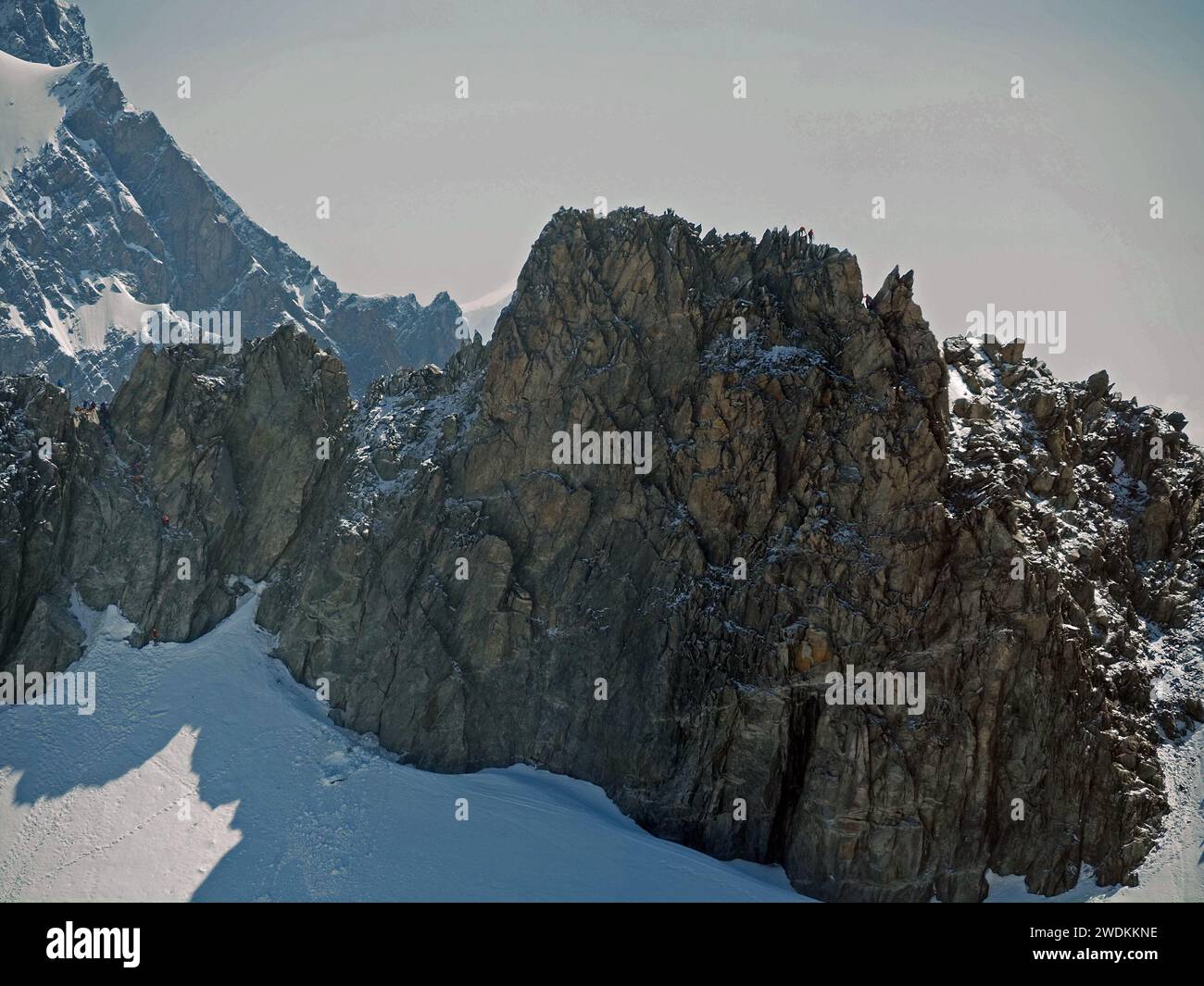 Blick auf winzige Ameisenkletterer auf einem Felsgrat mit Fußspuren im Schnee unter Felsen in der Region Monte Bianco (Mont Blanc) der italienischen Alpen Stockfoto