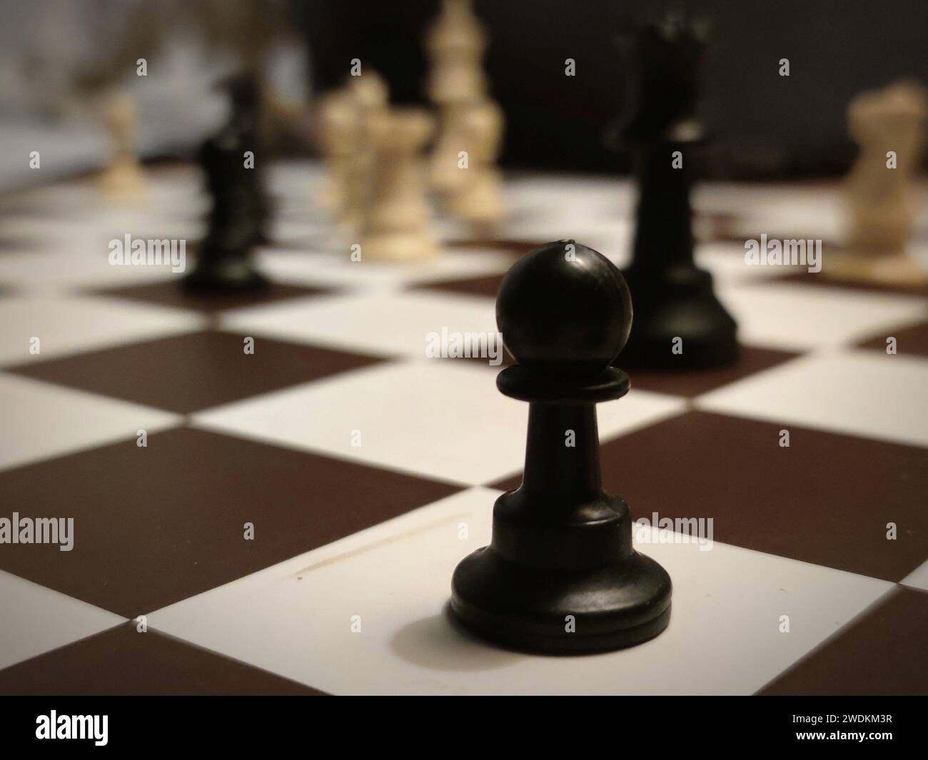 Detailliertes Bild eines schwarzen Bauern auf einem Schachbrett mit anderen Schachfiguren im Hintergrund. Stockfoto