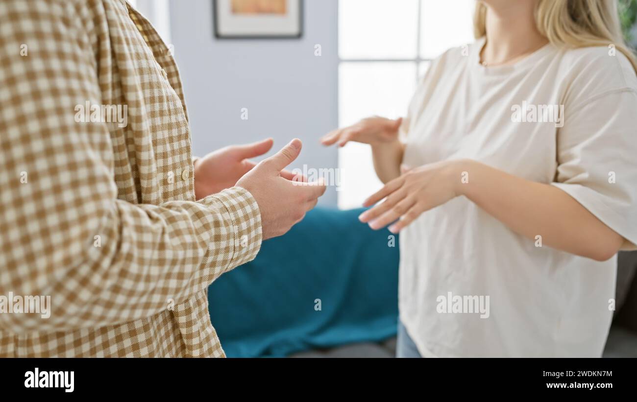 Ein Mann und eine Frau kommunizieren durch Handgesten in einem gemütlichen Wohnzimmer, wodurch die Verbindung im Wohnraum hervorgehoben wird. Stockfoto