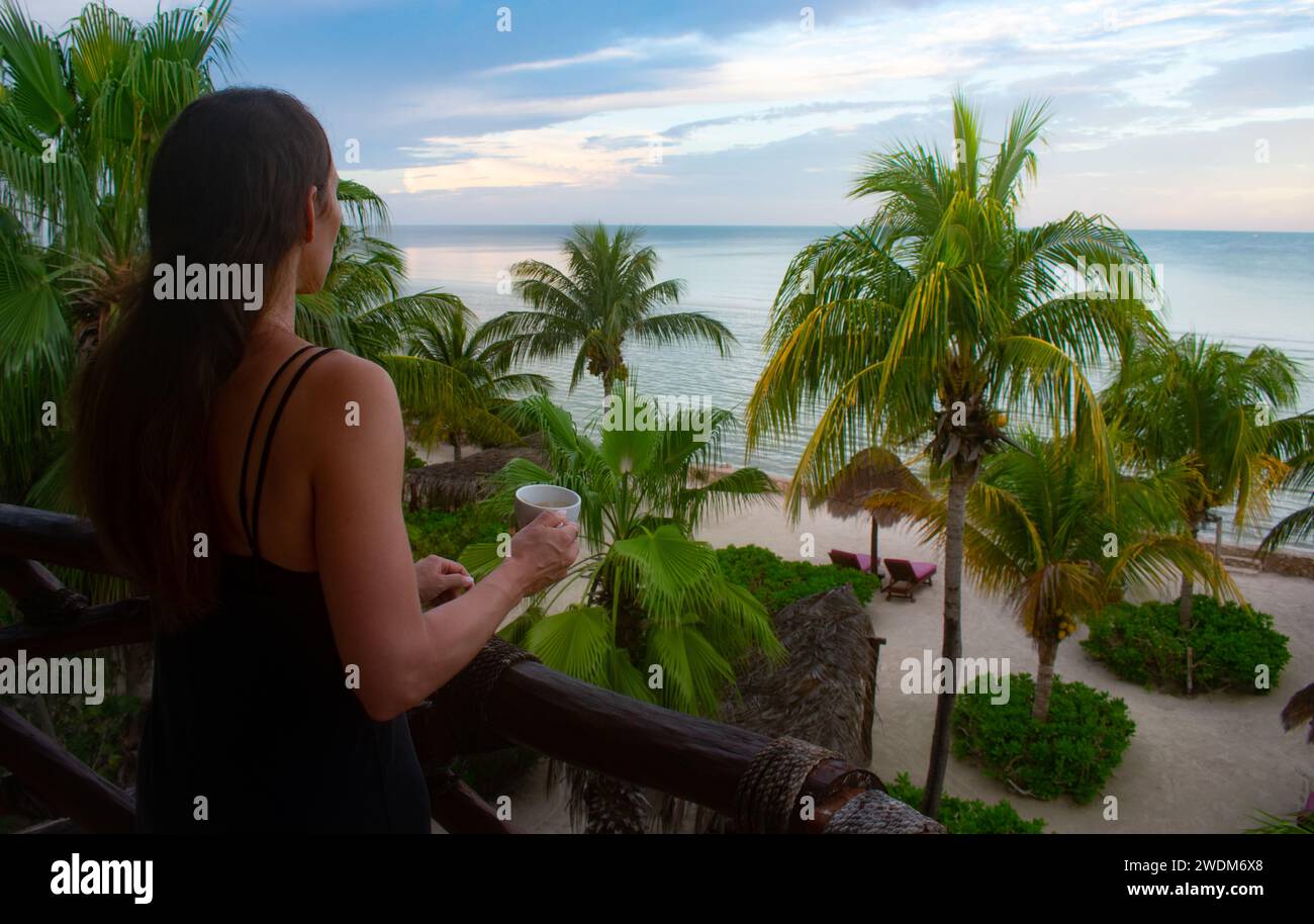 Frau genießt den Sonnenaufgang und Kaffee von einem Balkon in Holbox Mexiko Stockfoto