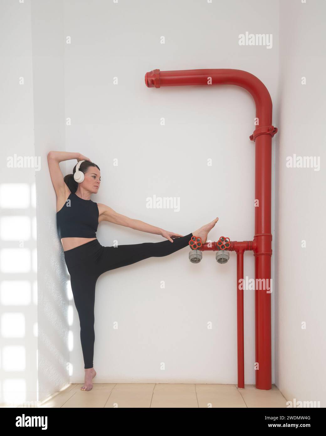 Eine sportliche Frau, die sich an den roten Rohren eines Hydranten ausdehnt Stockfoto