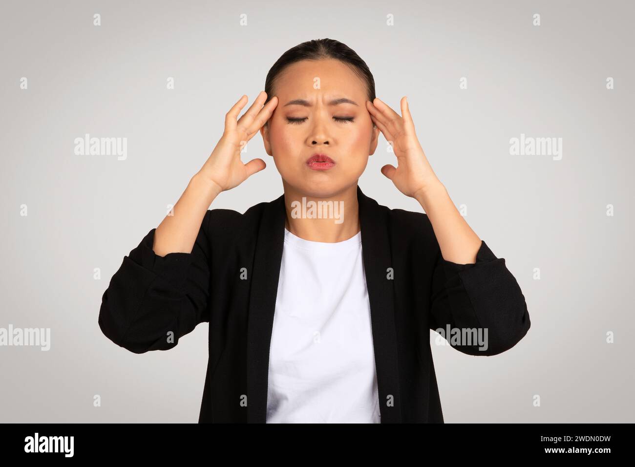 Eine gestresste asiatische Geschäftsfrau mit einem schmerzhaften Ausdruck, der den Kopf hält Stockfoto