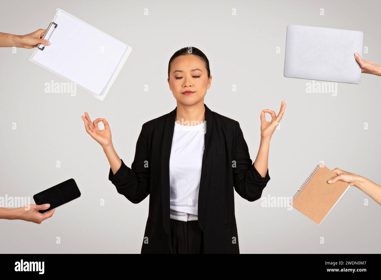 Ruhige asiatische Geschäftsfrau in meditativer Pose, umgeben von Bürogegenständen Stockfoto