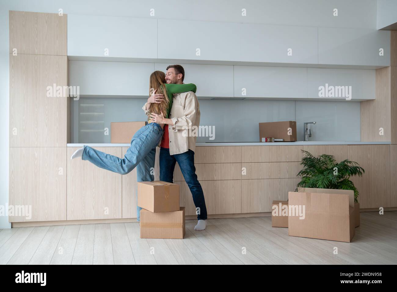 Glückliche Frau, die einen lächelnden, freudigen Ehemann am Umzugstag in ein neues Apartment, ein Haus, eine Wohnung umschließt Stockfoto