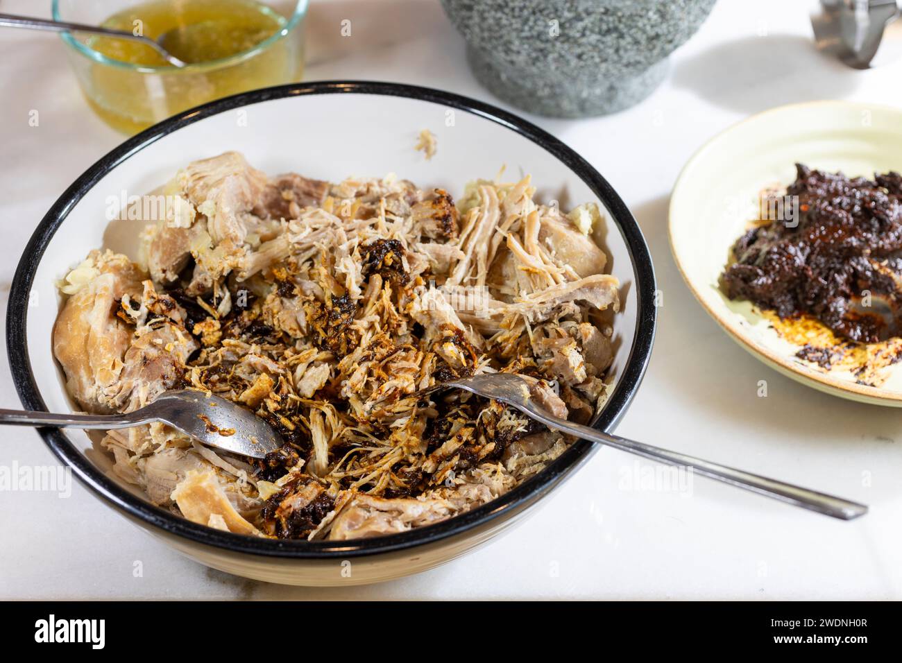 Kochen und Verarbeiten von Pulled Schweinefleisch mit roter Anchochili-Paste und Schweinefleisch auf einem Schneidebrett aus weißem Marmor Stockfoto