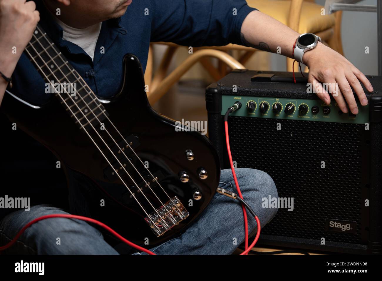 latein-Mann, der einen Verstärker anschaltet, um einen E-Bass zu spielen, Selbstlerner Stockfoto