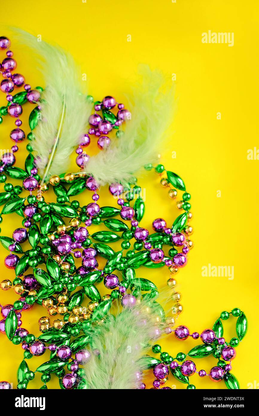 Mardi Gras Konzept. Mehrfarbige Perlen auf gelbem Hintergrund. Festliche Karnevalssymbole. Goldene grüne und lila Dekoration für den Urlaub. Vertikales Foto Stockfoto