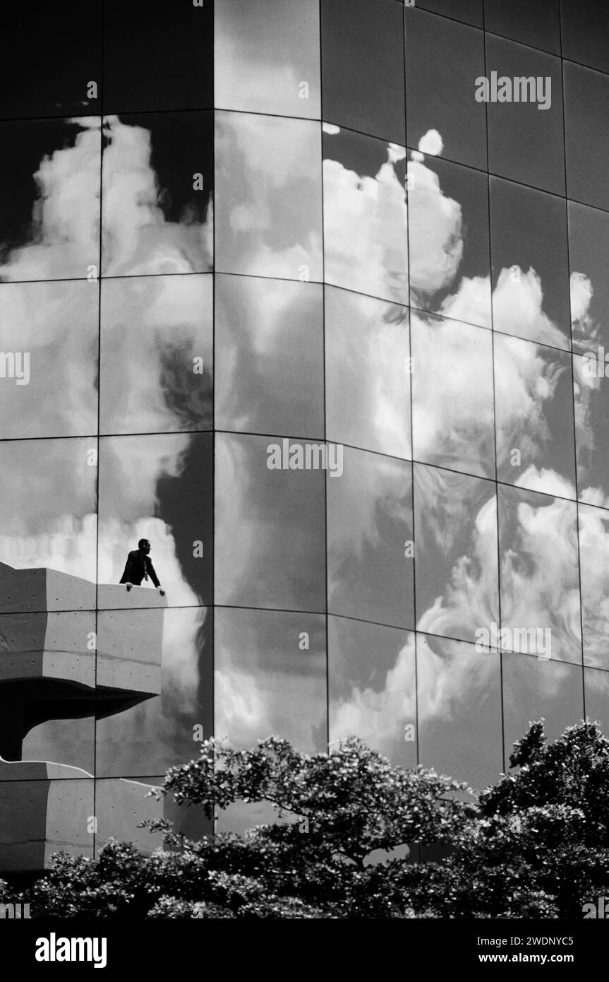 Ein schwarz-weiß-Foto von Valon Geschäftsmann, der auf einem Balkon vor dem Auto-Glas-Gebäude steht, mit Wolken reflektieren Stockfoto