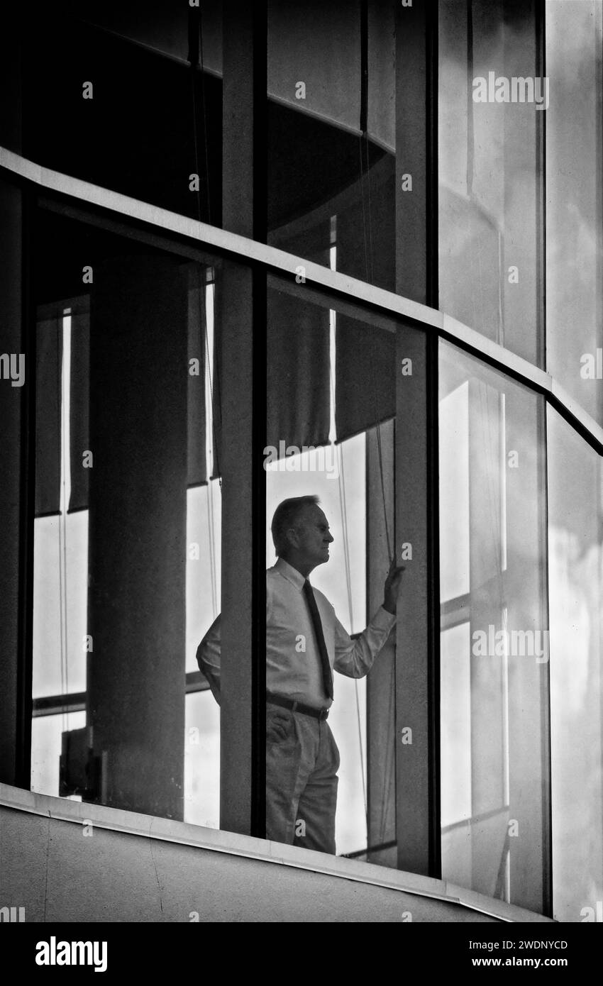 Ein Schwarzweiß-Foto von einem Geschäftsmann, der aus seinem Hochhaus des Firmenbüros starrt Stockfoto