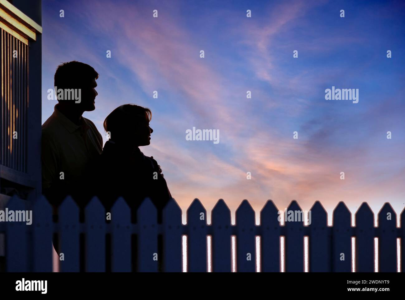 Silhouette eines jungen Paares, das den wunderschönen Sonnenuntergang am Abend mit einem Pflückzaun im Vordergrund beobachtet Stockfoto