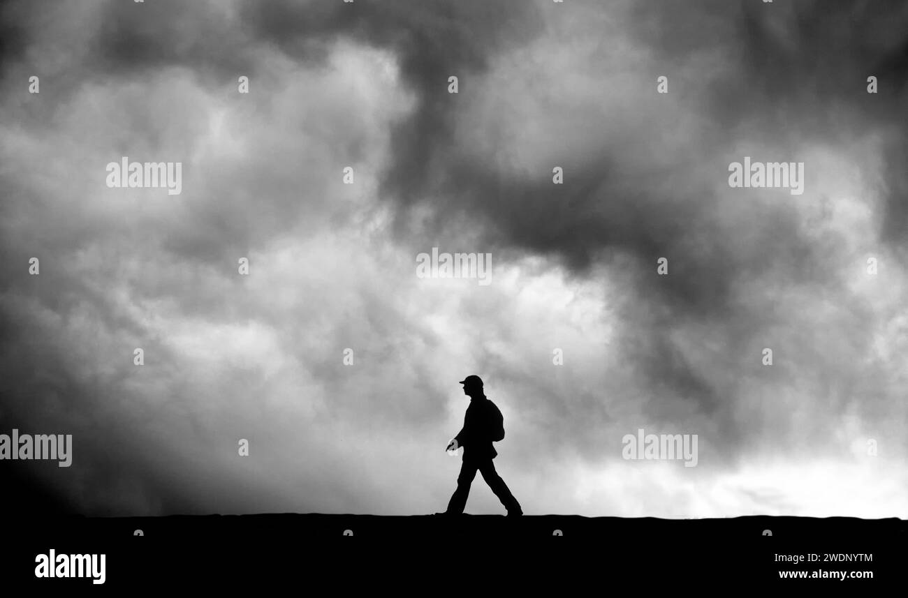 Die Silhouette einer Person, die im Rucksack läuft, vor dem Hintergrund wütender, bedrohlicher Sturmwolken Stockfoto